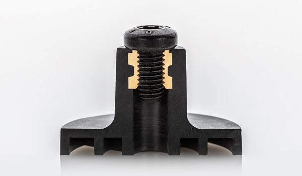 Primer plano de un inserto roscado o perno de inserción en un componente de plástico negro. El tornillo está firmemente anclado en el plástico y permite una unión resistente y repetidamente desmontable a largo plazo.